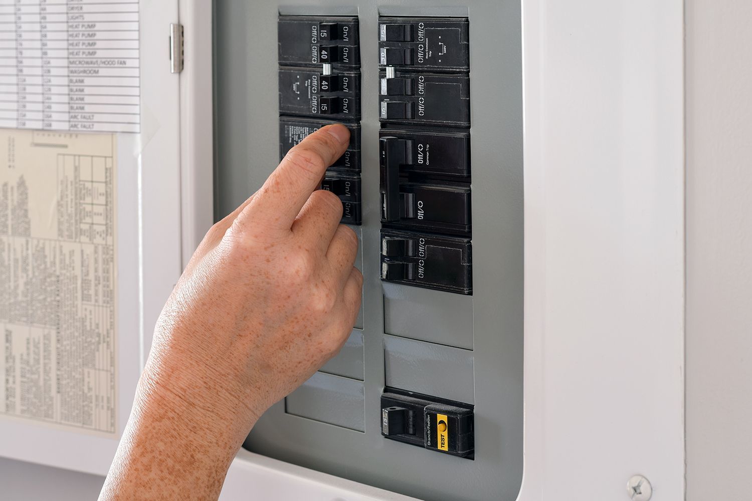 Hand adjusting a breaker switch in an electrical panel