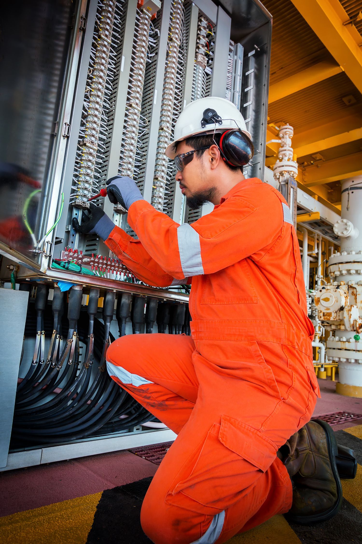 Worker in orange coveralls adjusting cables on industrial equipment, wearing a hard hat and gloves.