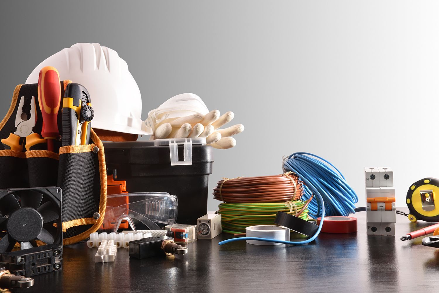 Construction tools and safety gear on a workbench, including gloves, hard hat, cables, and tape measure