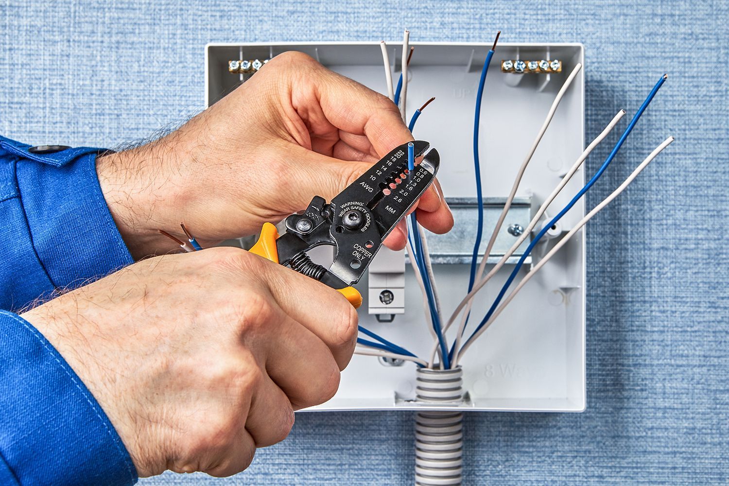Hands wiring an electrical box with blue cables using wire strippers