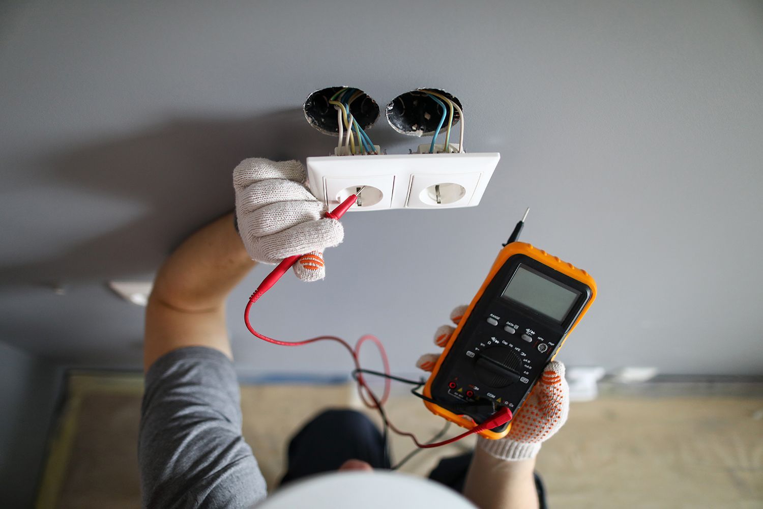 Electrician testing a ceiling light fixture with a multimeter and red wires Electrician testing a ceiling light fixture with a multimeter and red wires