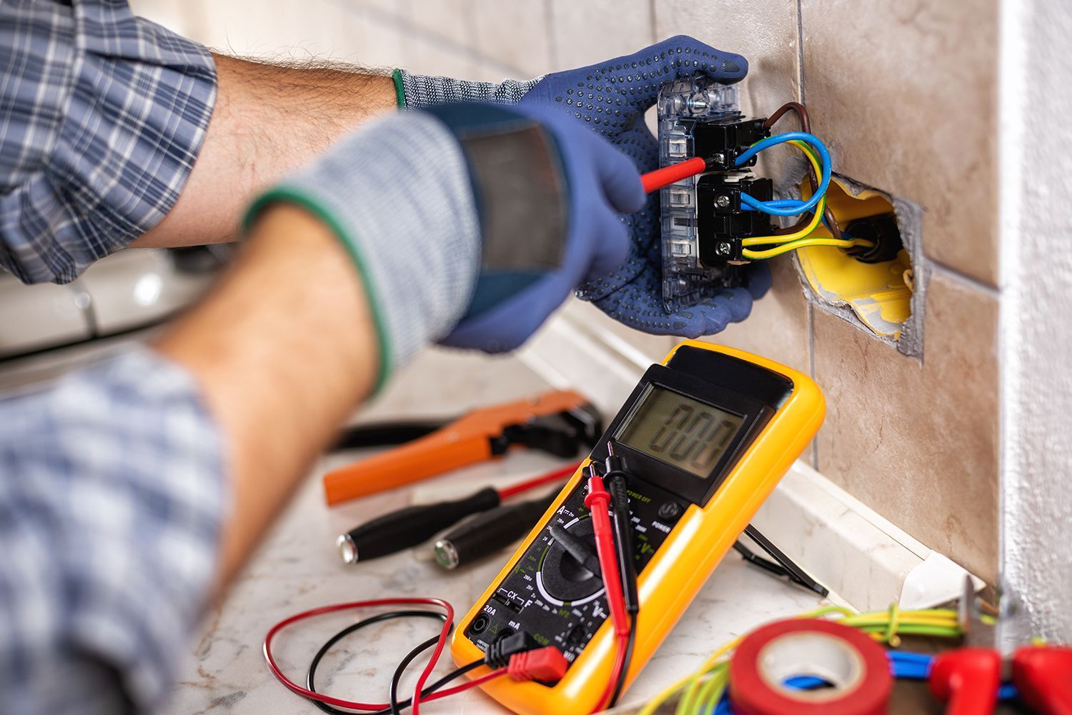 Electrician wiring a wall outlet with tools and a multimeter nearby Electrician wiring a wall outlet with tools and a multimeter nearby