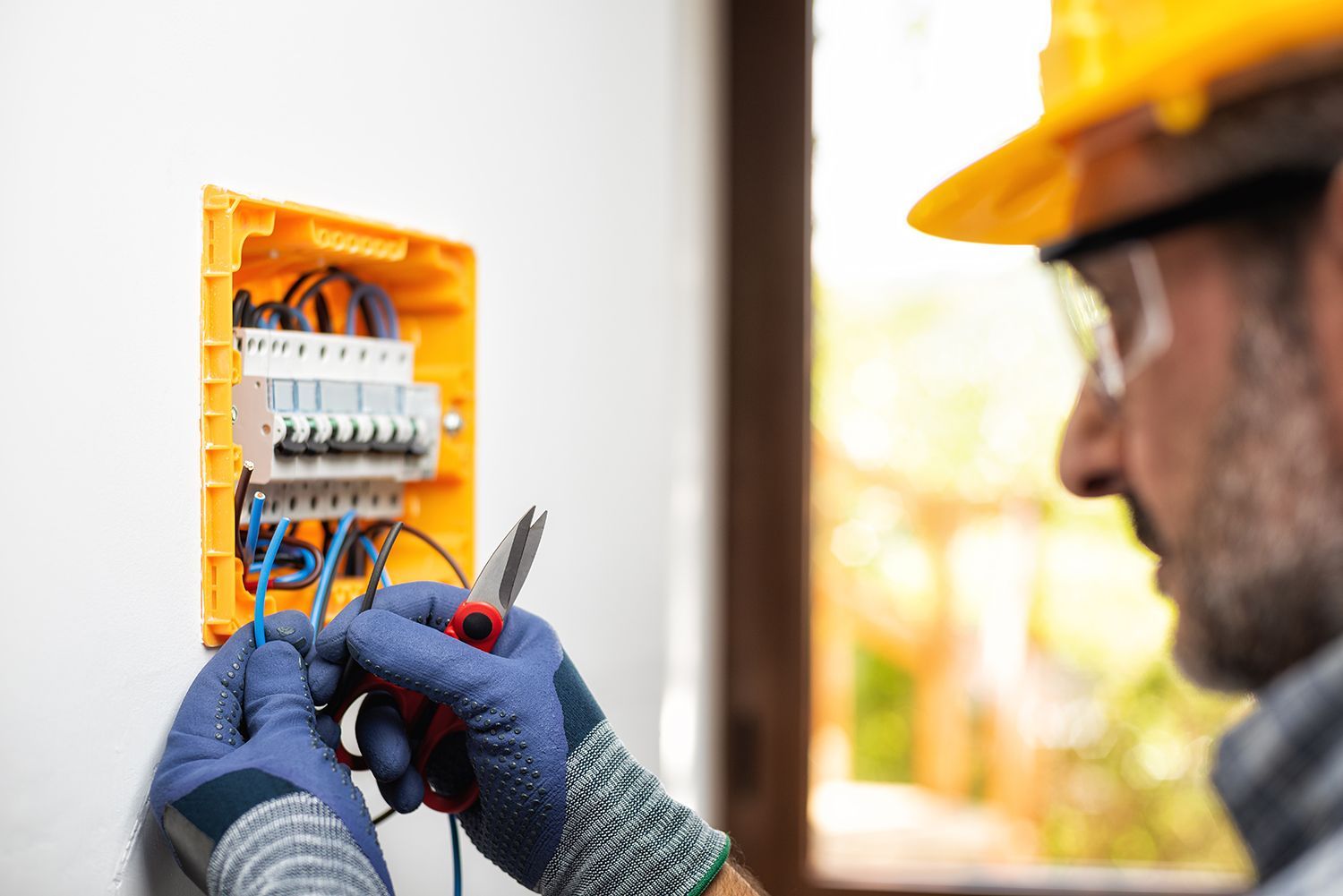 Electrician wiring an open orange circuit panel while wearing gloves and a hard hat Electrician wiring an open orange circuit panel while wearing gloves and a hard hat