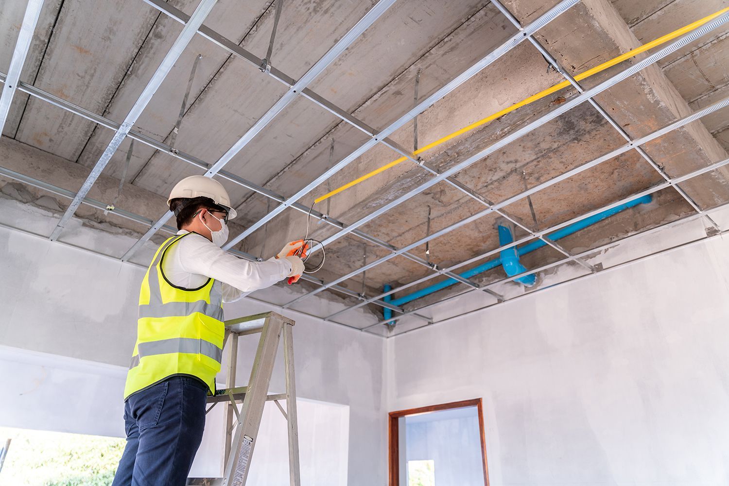 Worker in a hard hat inspecting ceiling pipes in a room under construction