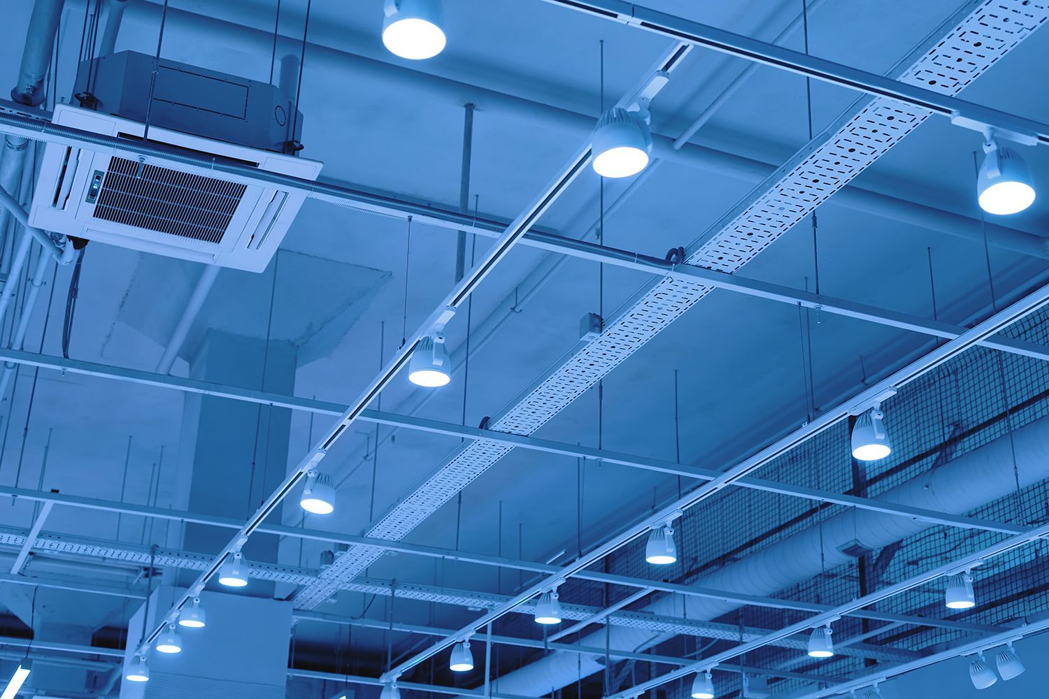 Blue-lit industrial ceiling with exposed beams, vents, ducts, and hanging lights
