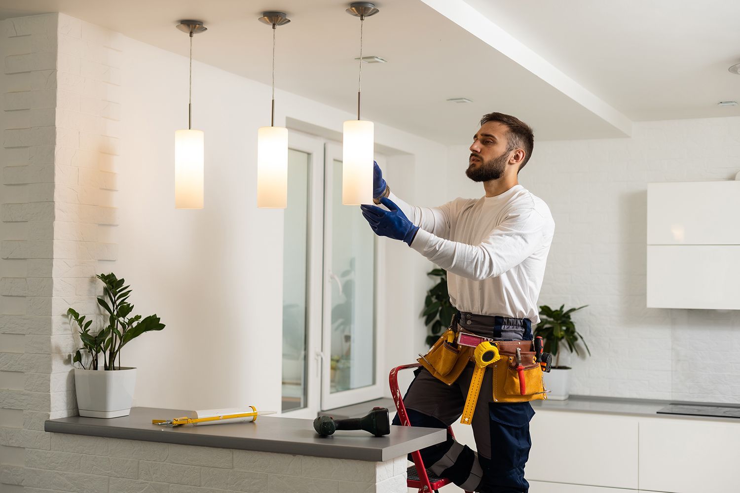 Electrician adjusting a ceiling light in a modern kitchen with tools on a counter Electrician adjusting a ceiling light in a modern kitchen with tools on a counter