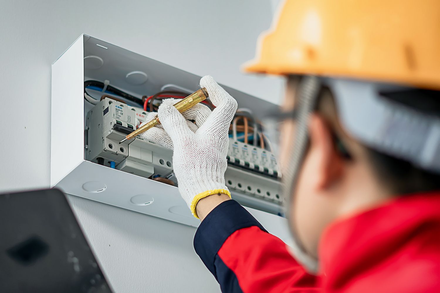 Technician wearing gloves adjusts wiring inside an open electrical panel
