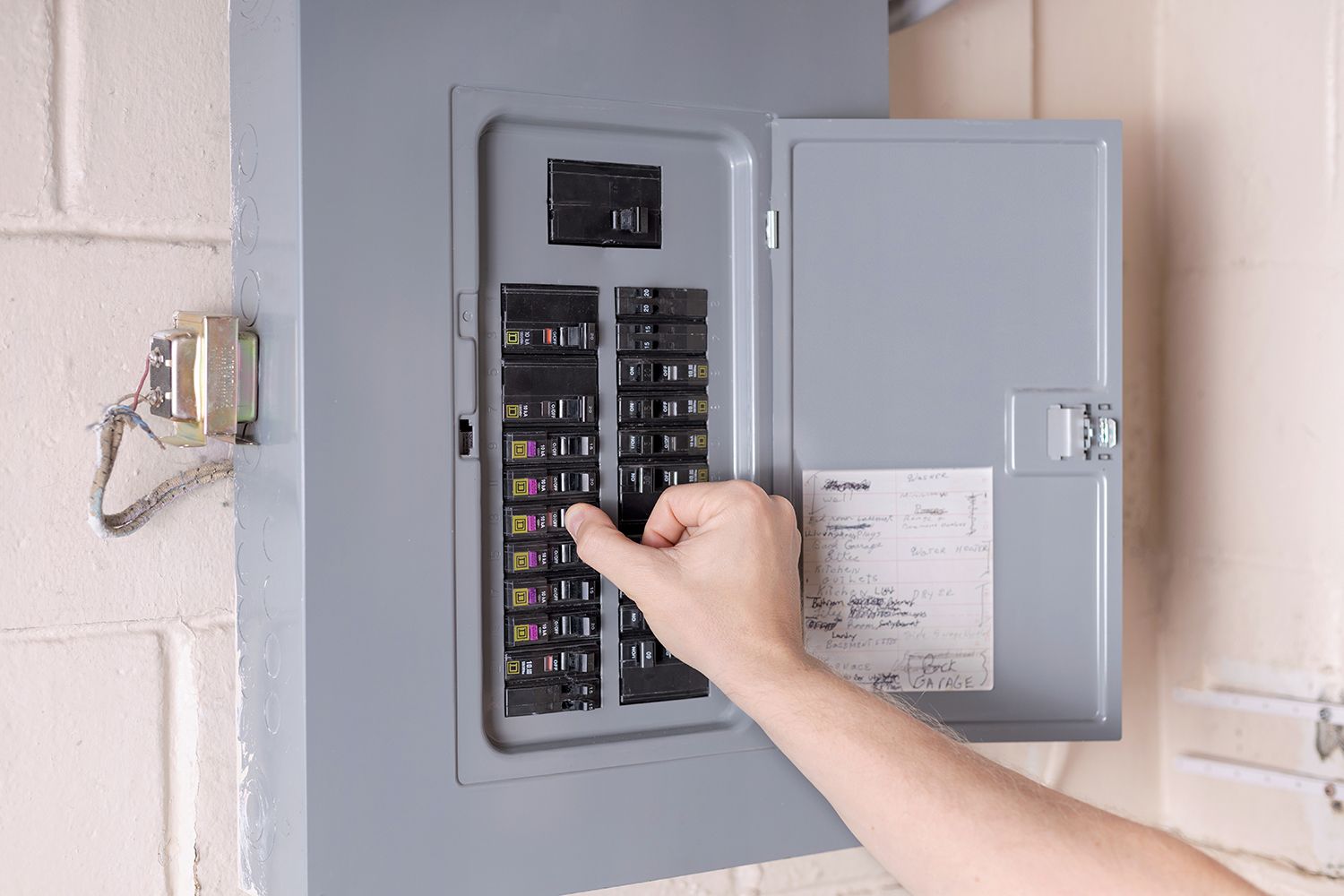 Hand opening a gray electrical breaker panel with labeled switches
