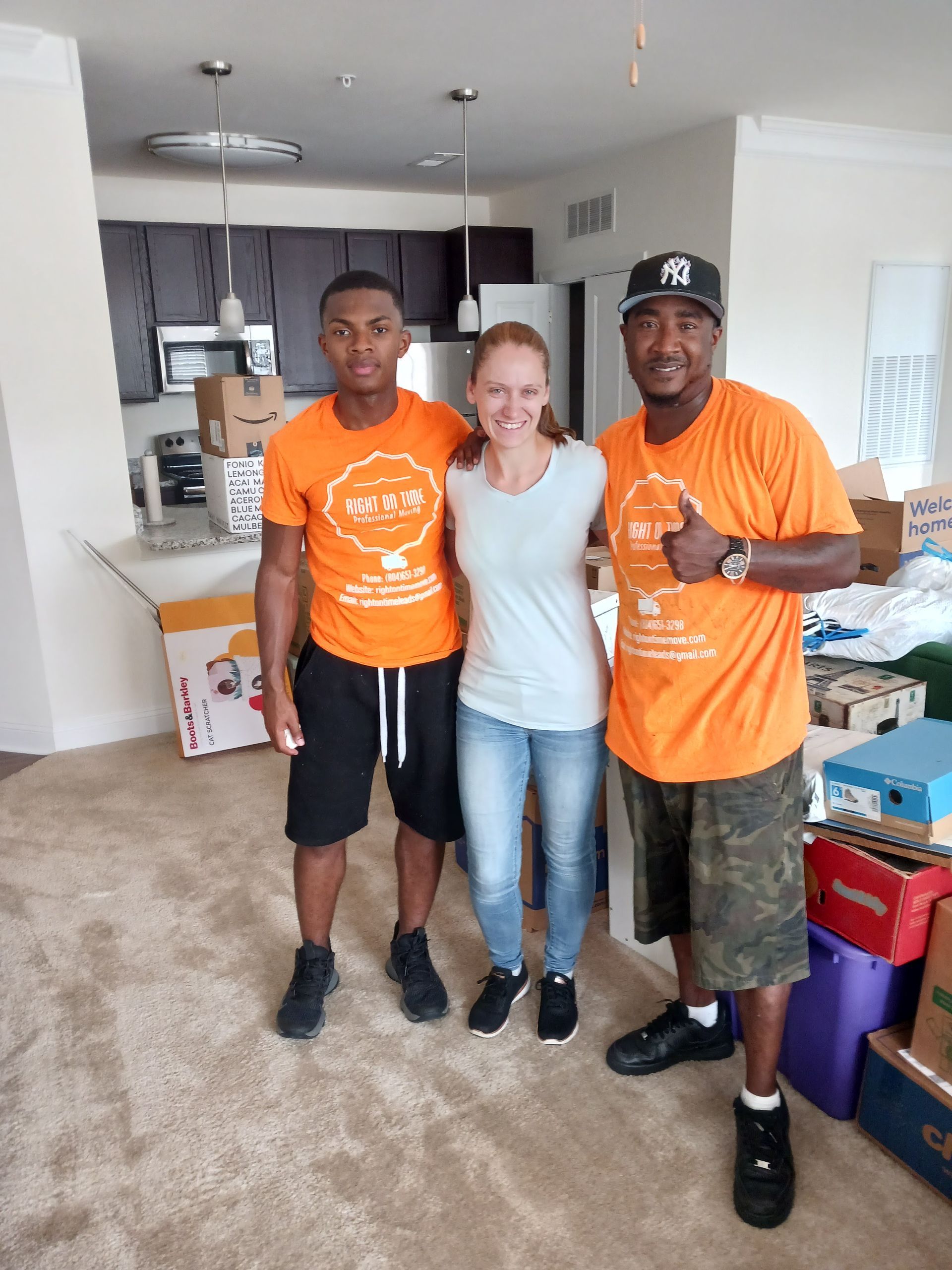 Three people standing in a living room, smiling and posing in orange and light blue shirts.
