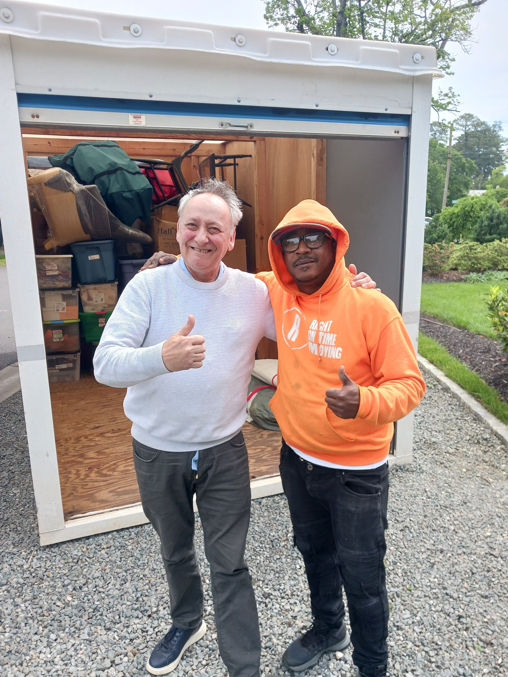 Two people smiling and giving thumbs up in front of an open storage unit in a parking lot
