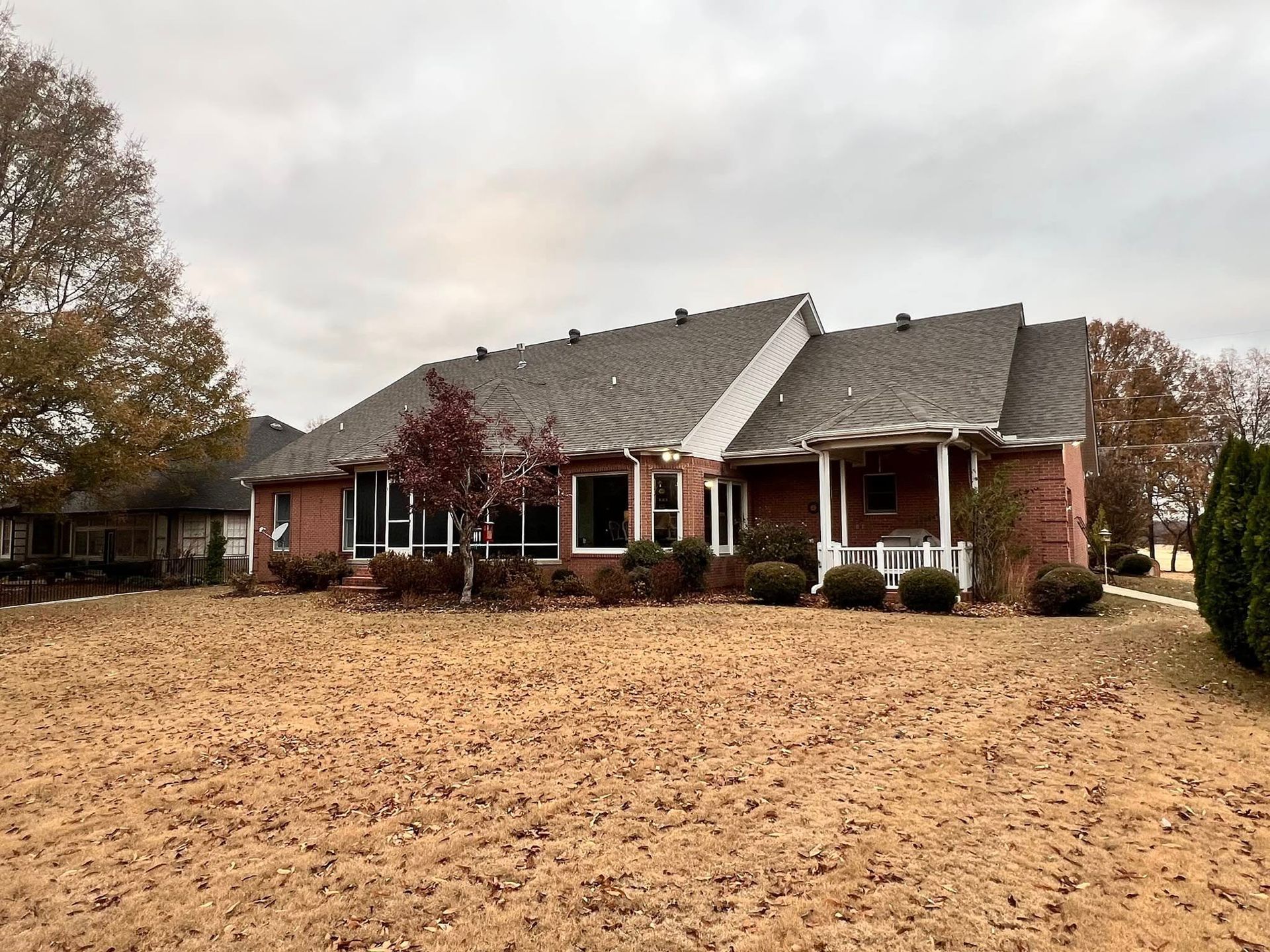 A large brick house with a gray roof is sitting on top of a dry grass field.