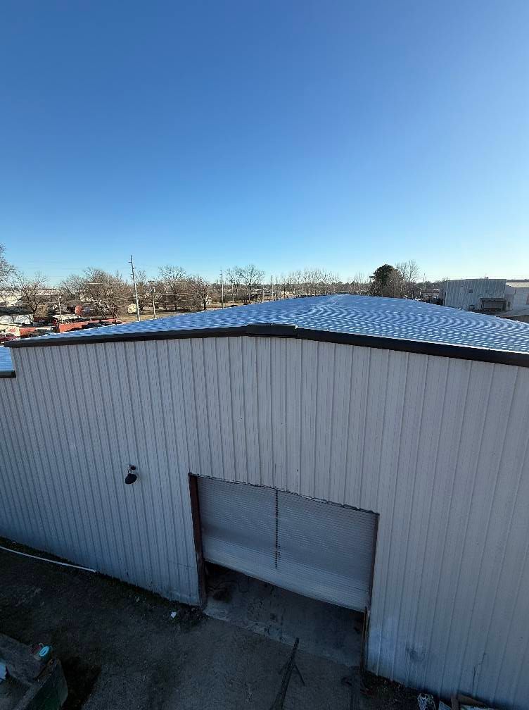 White industrial building with open loading door, snow-covered roof, and clear blue sky.