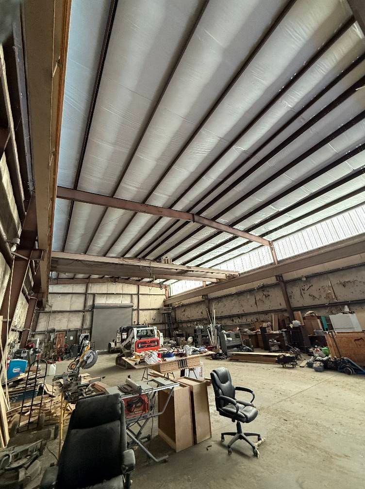 Large metal workshop interior with a corrugated ceiling and various tools/equipment.