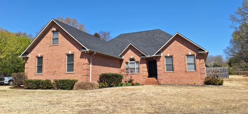 Brick house with black roof under a clear blue sky. A grassy yard is in the foreground.
