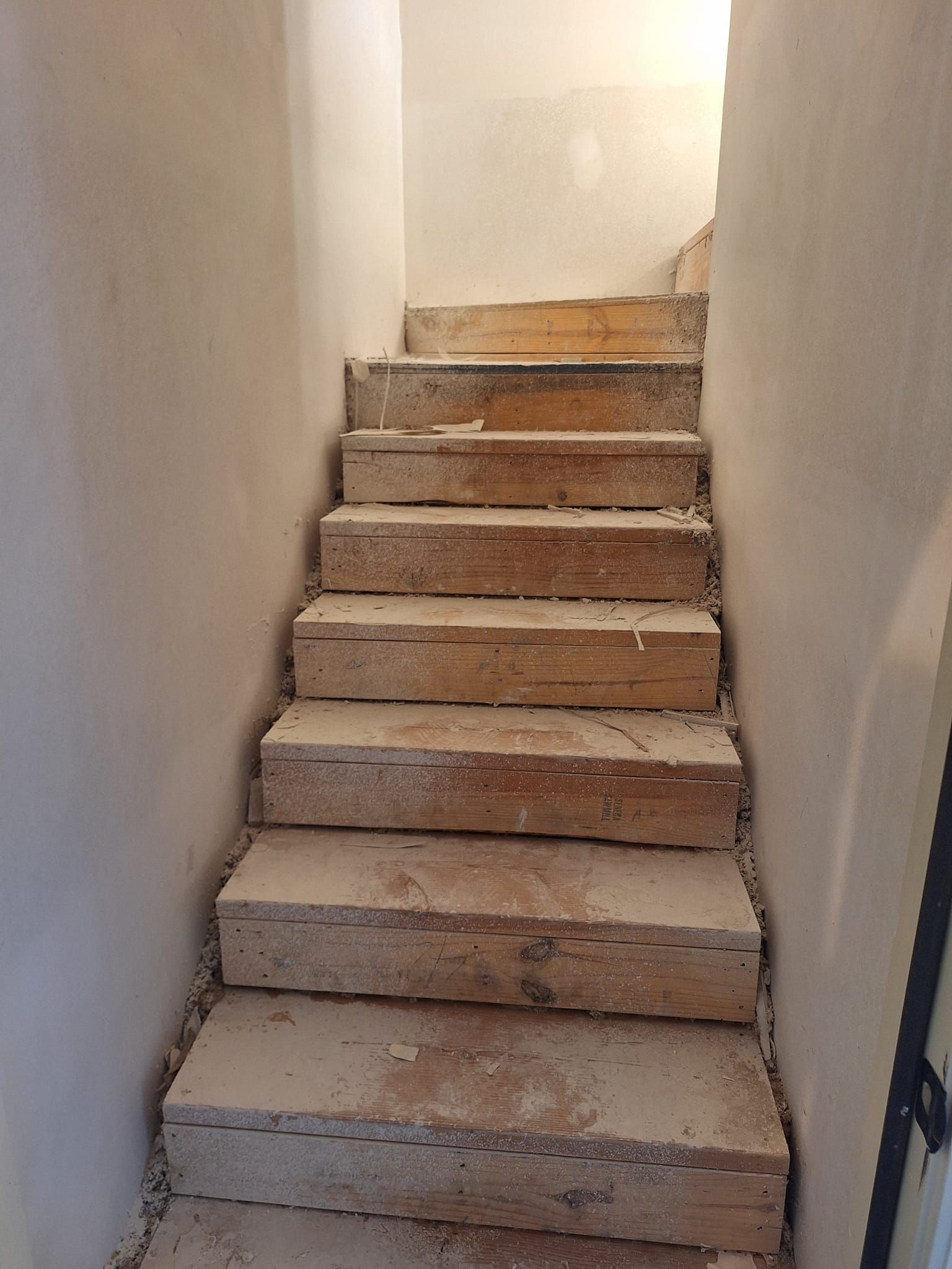 Wooden stairs under construction, set between white walls.