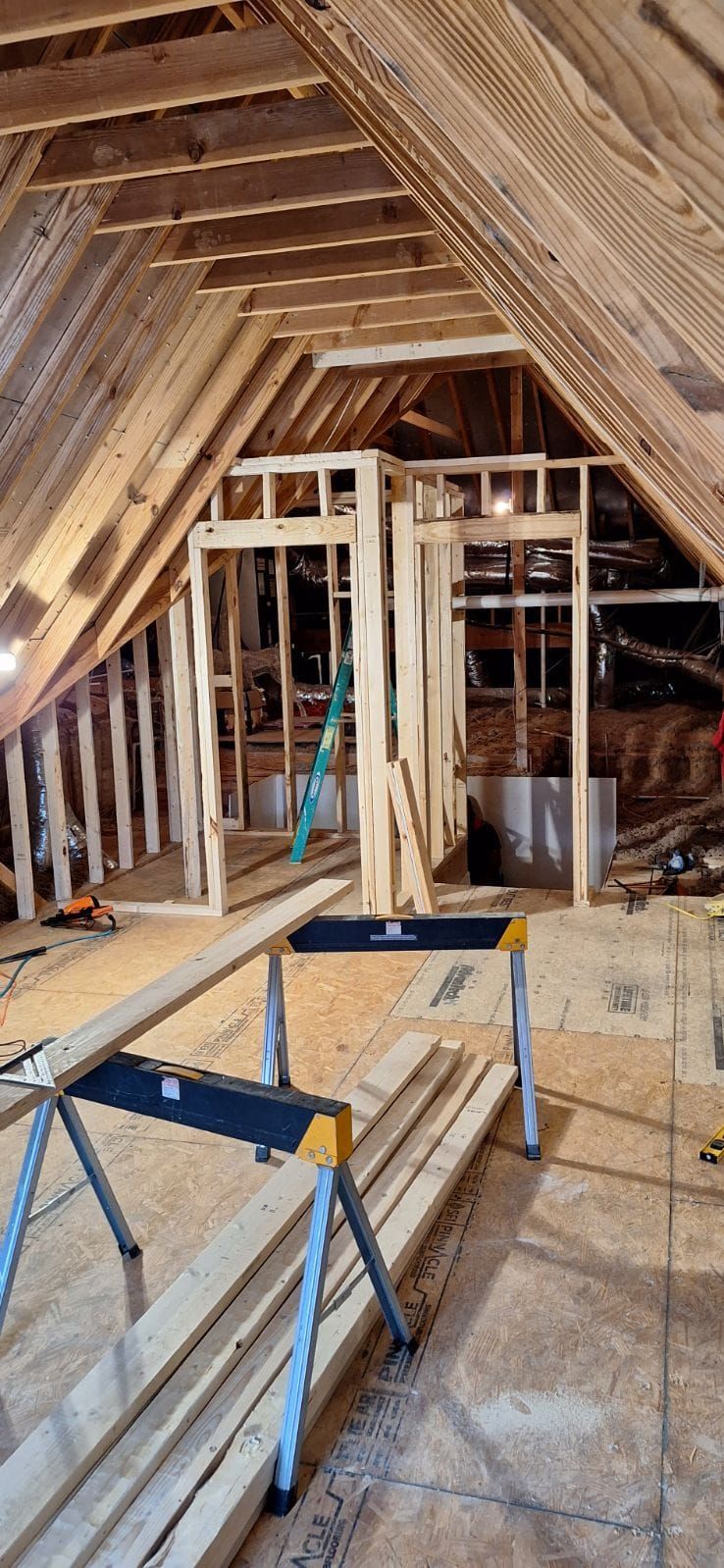 Interior view of a wooden attic under construction with exposed beams, framing, and sawhorses.