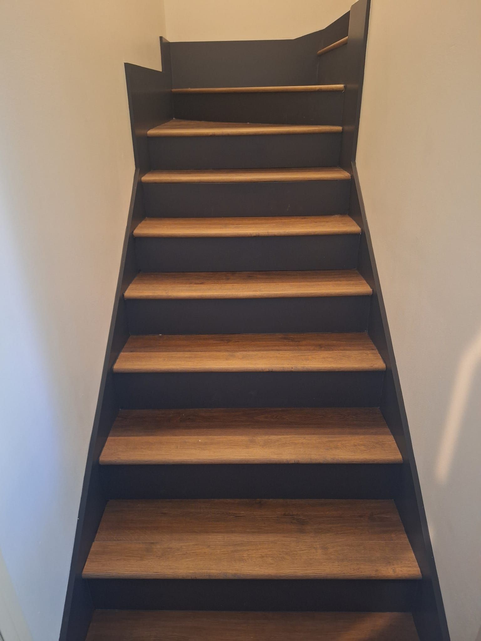 Staircase with wooden steps and dark gray risers and side panels against a white wall.