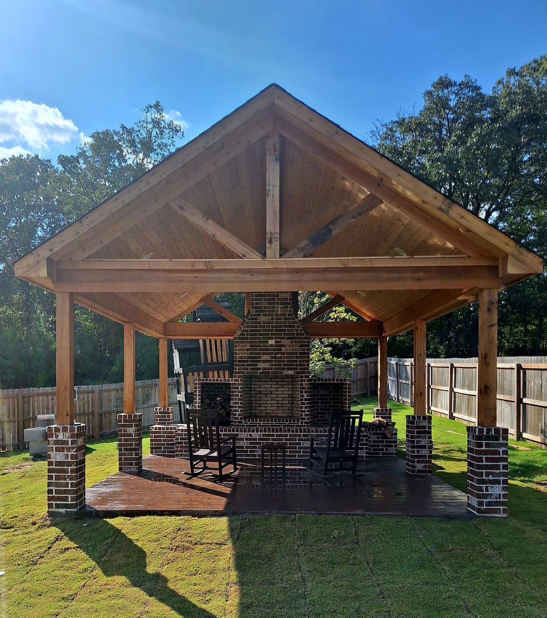 Wooden pavilion with brick fireplace and pillars on a grassy lawn.