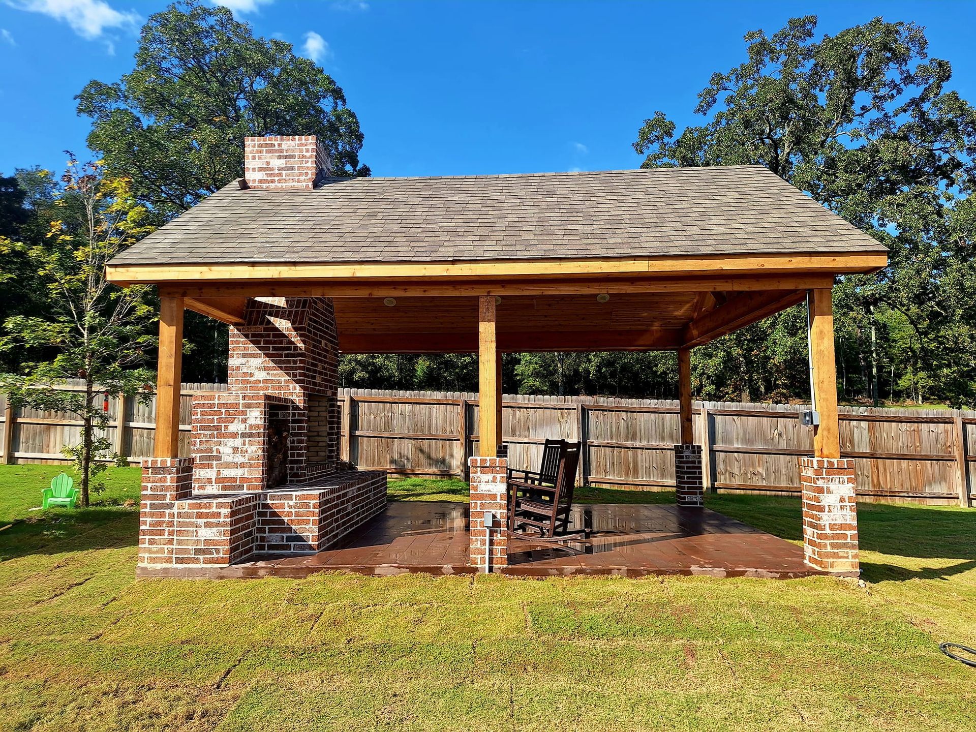 A brick pavilion with a wooden roof and a fireplace in the backyard.