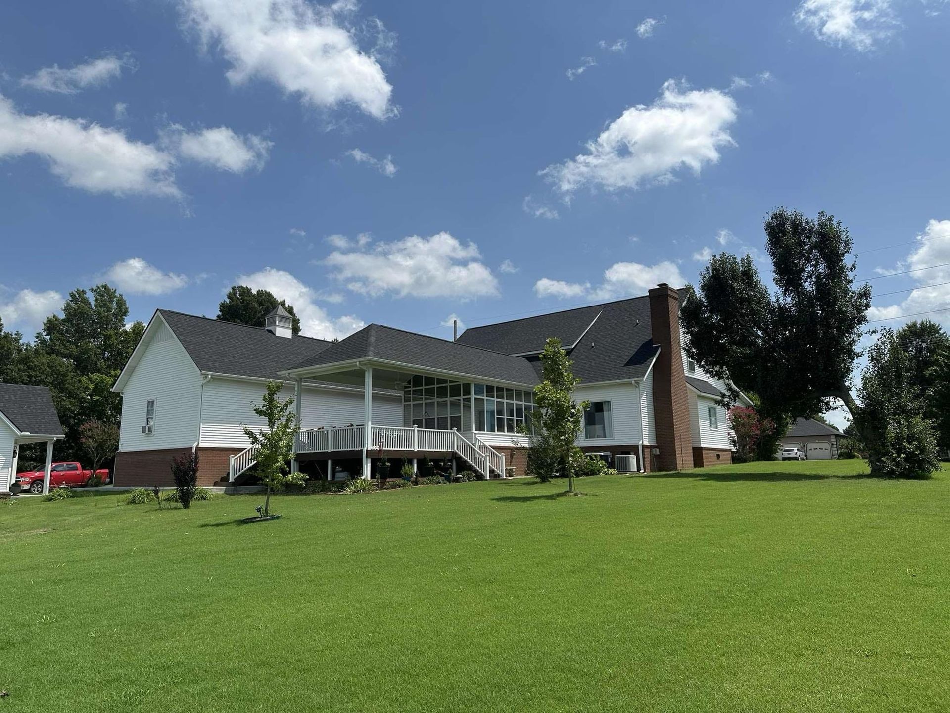 White house with dark roof and brick chimney against a blue sky with fluffy white clouds, green lawn.