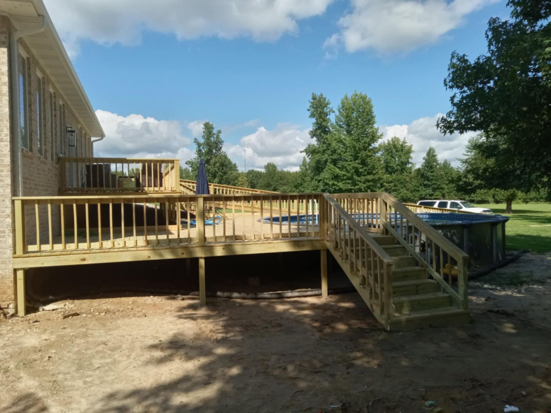 Wooden deck with steps next to a house and above-ground pool on a sunny day.