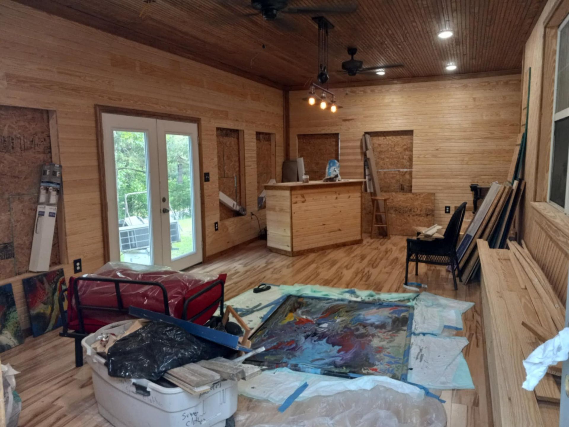 Interior room under construction, with wood paneling, French doors, and a bar. Construction materials are scattered.