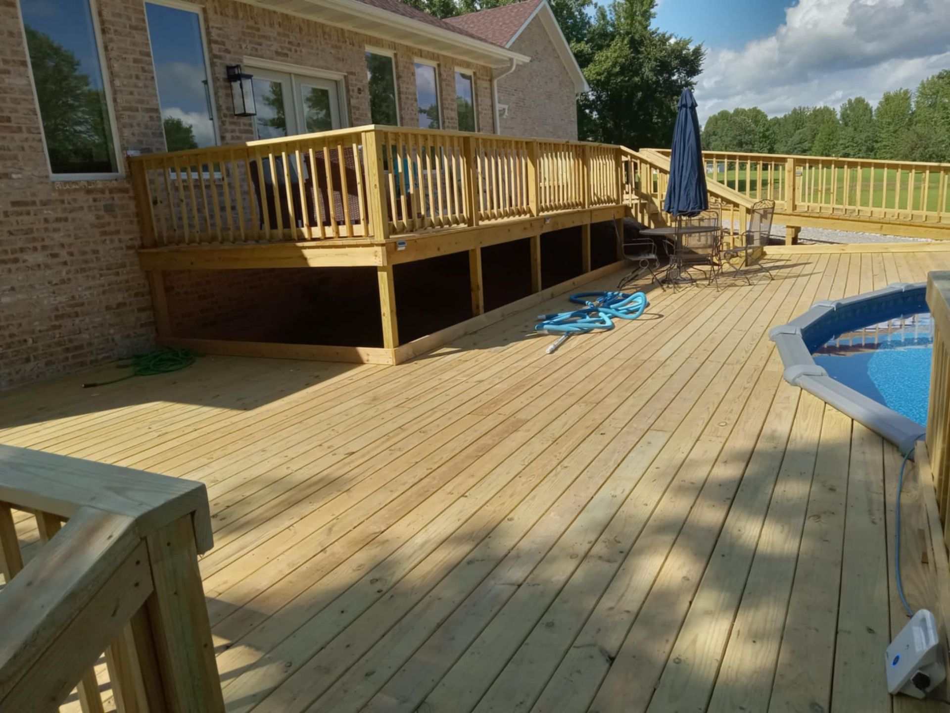 Wooden deck attached to a brick house, next to a pool.