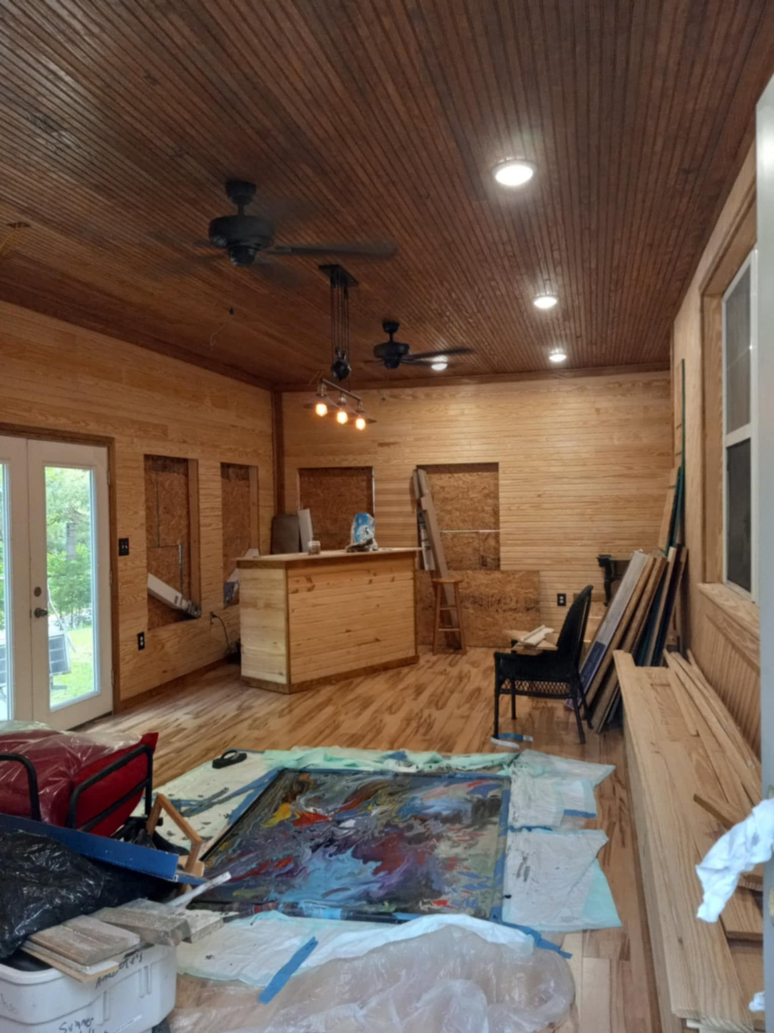 Interior view of a wood-paneled room, with unfinished walls, a bar, and art supplies.