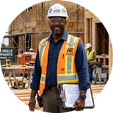 Construction worker in hard hat and safety vest holding papers at a building site