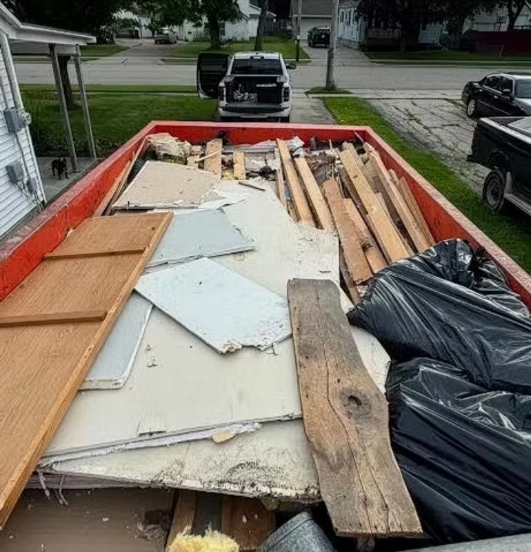 Large black dumpster on a driveway in a suburban neighborhood at dusk.