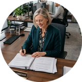 Woman signing paperwork at an office desk with a smiling expression