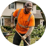 Worker in orange safety shirt raking leaves in a suburban yard near a house