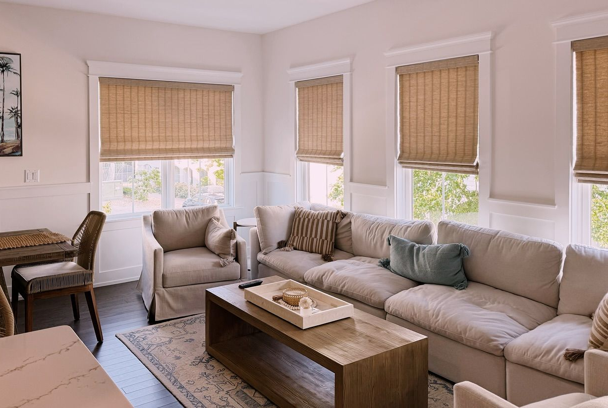 Living room with sectional sofa, wooden coffee table, woven shades, and natural light.