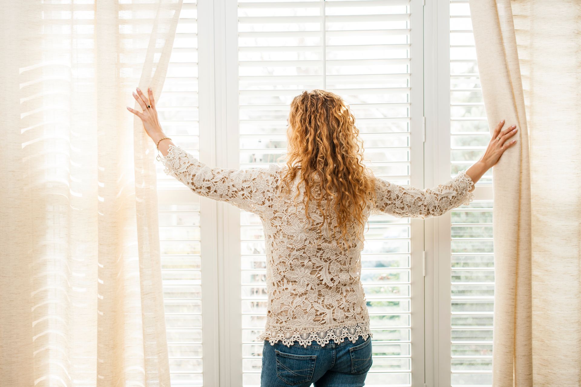 Person opening shutters and curtains to add sunlight into their living room at Designing Windows