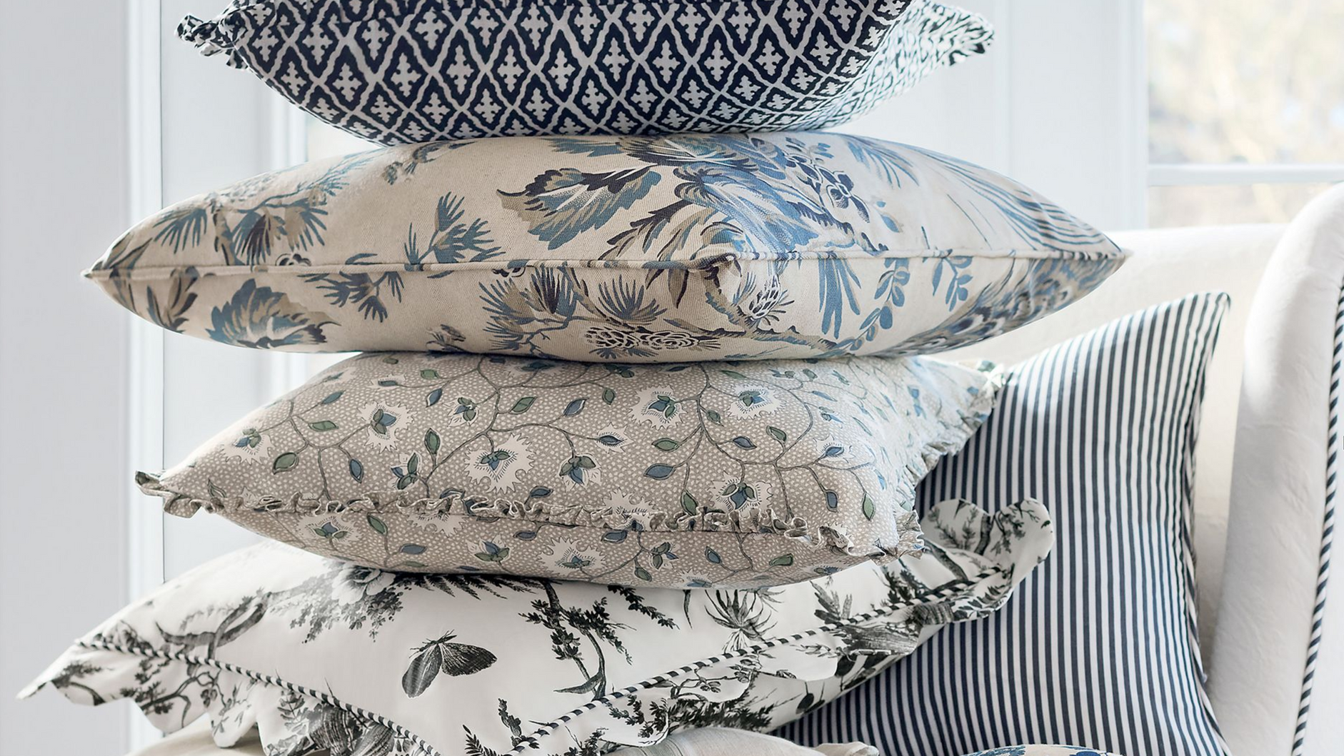 Stack of blue and white patterned throw pillows on a white chair.