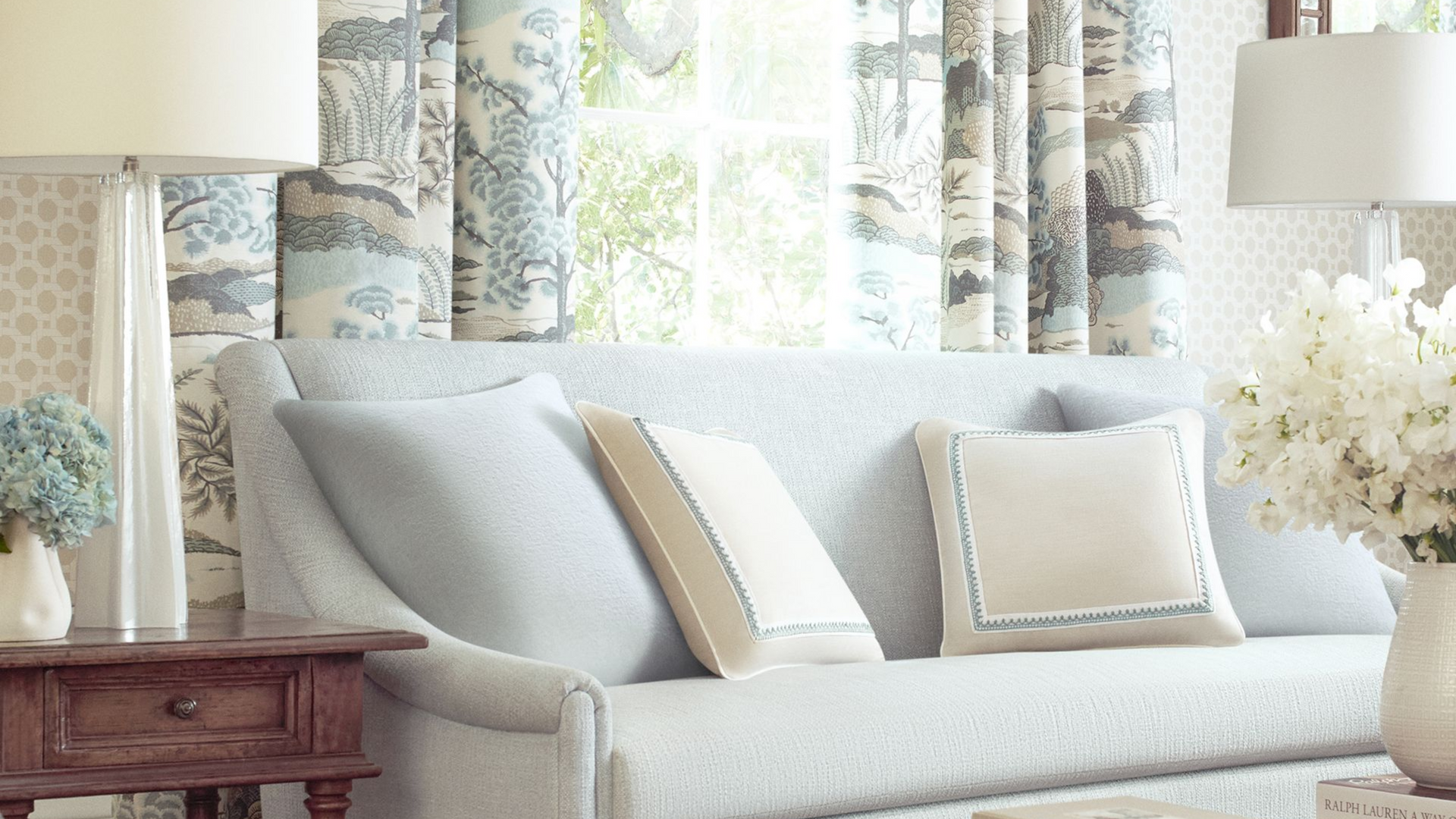 Living room with a light blue sofa, patterned curtains, and floral decor.