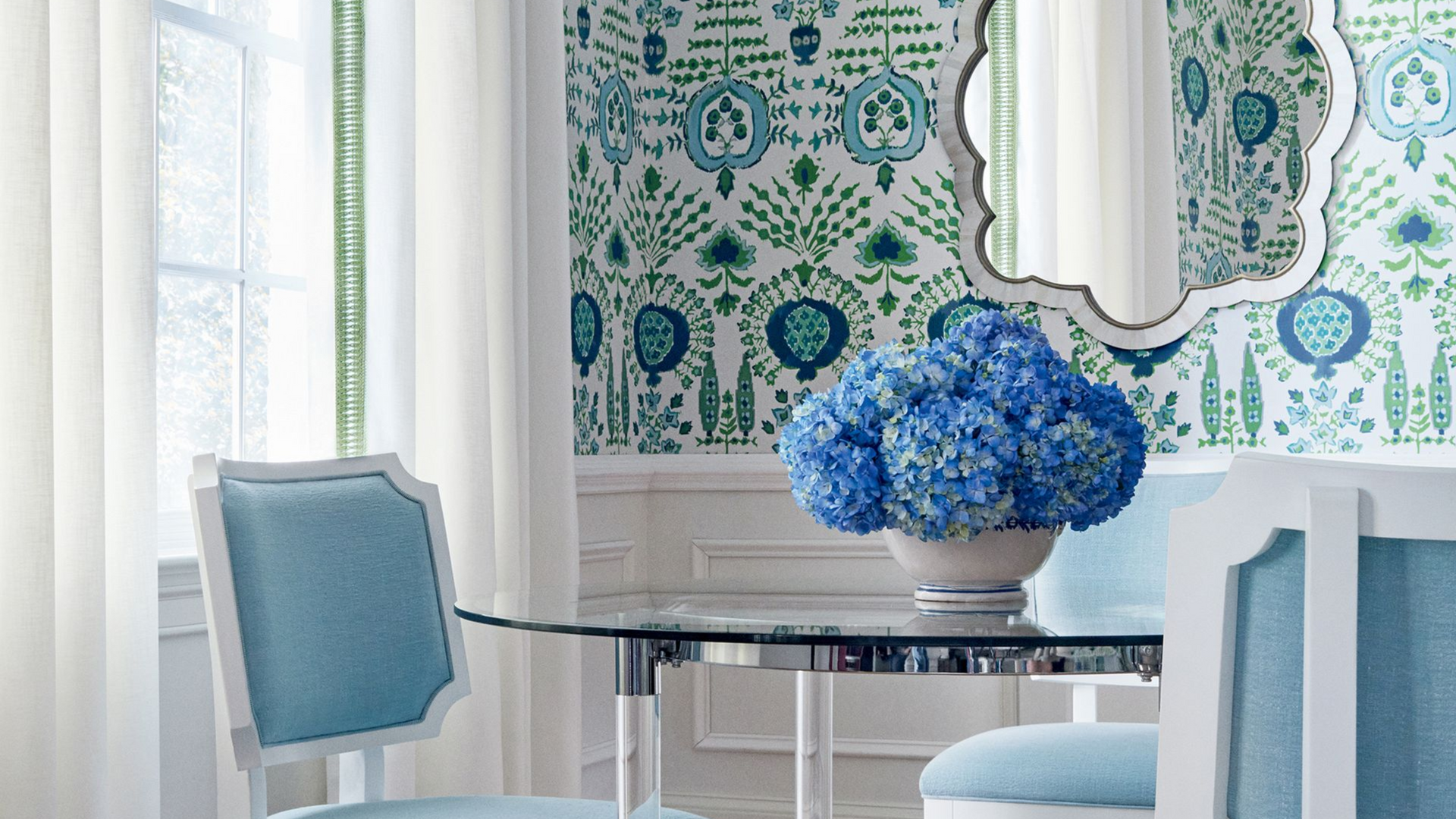 Dining room with blue and white decor. Round glass table, chairs, floral wallpaper, and hydrangea centerpiece.