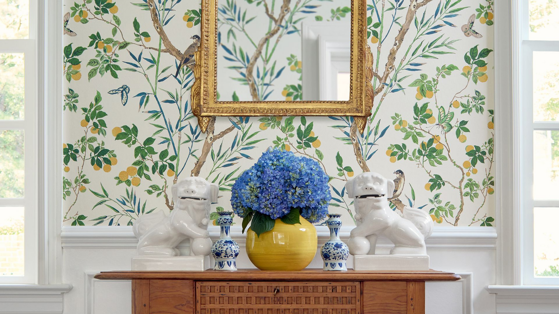 Room with floral wallpaper, gold mirror, blue flowers, and white figurines.
