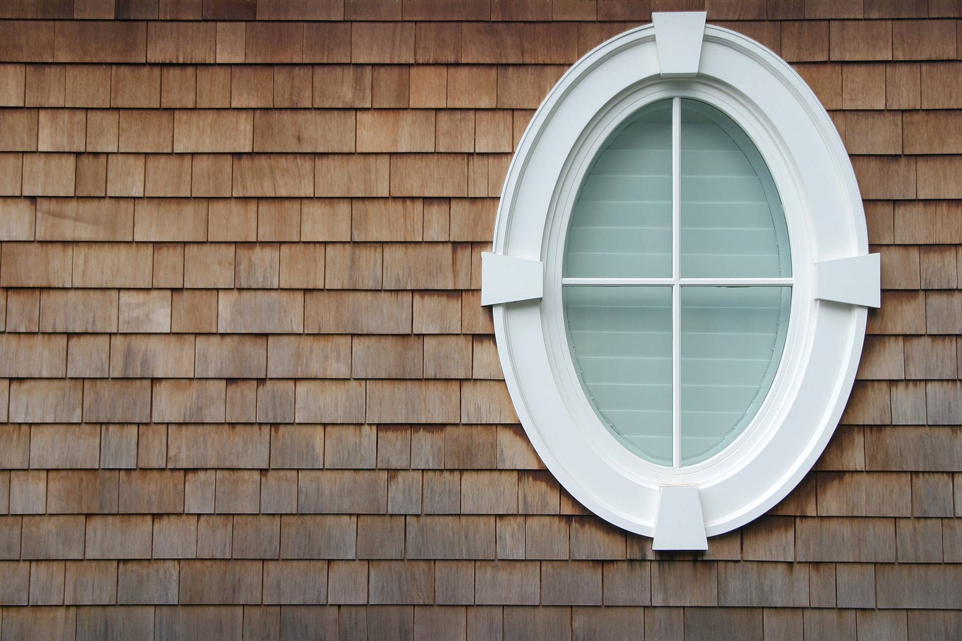 An oval window with interior shutters seen from the exterior of a residential home