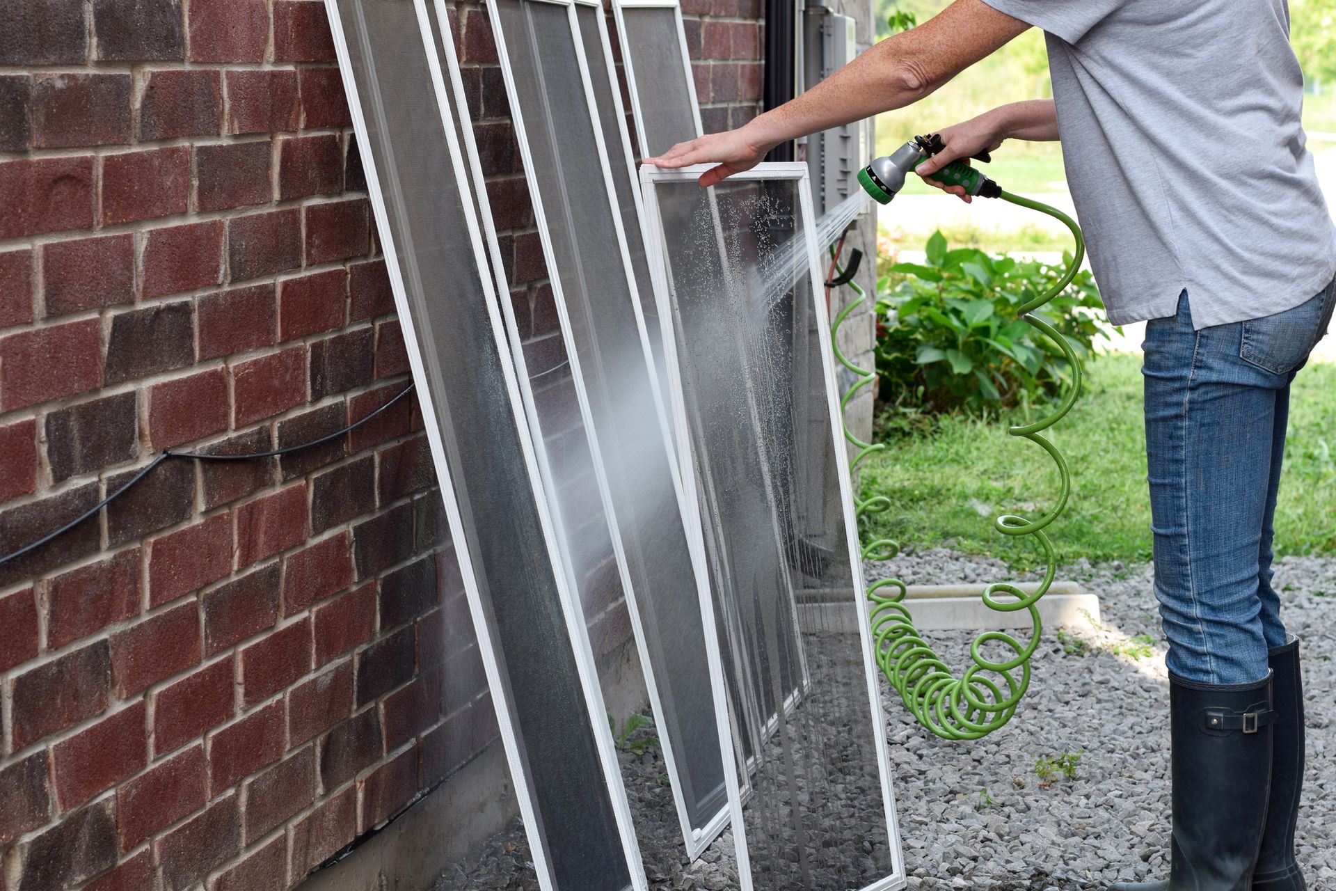 Person washing a window leaning against a brick wall with a hose outdoors