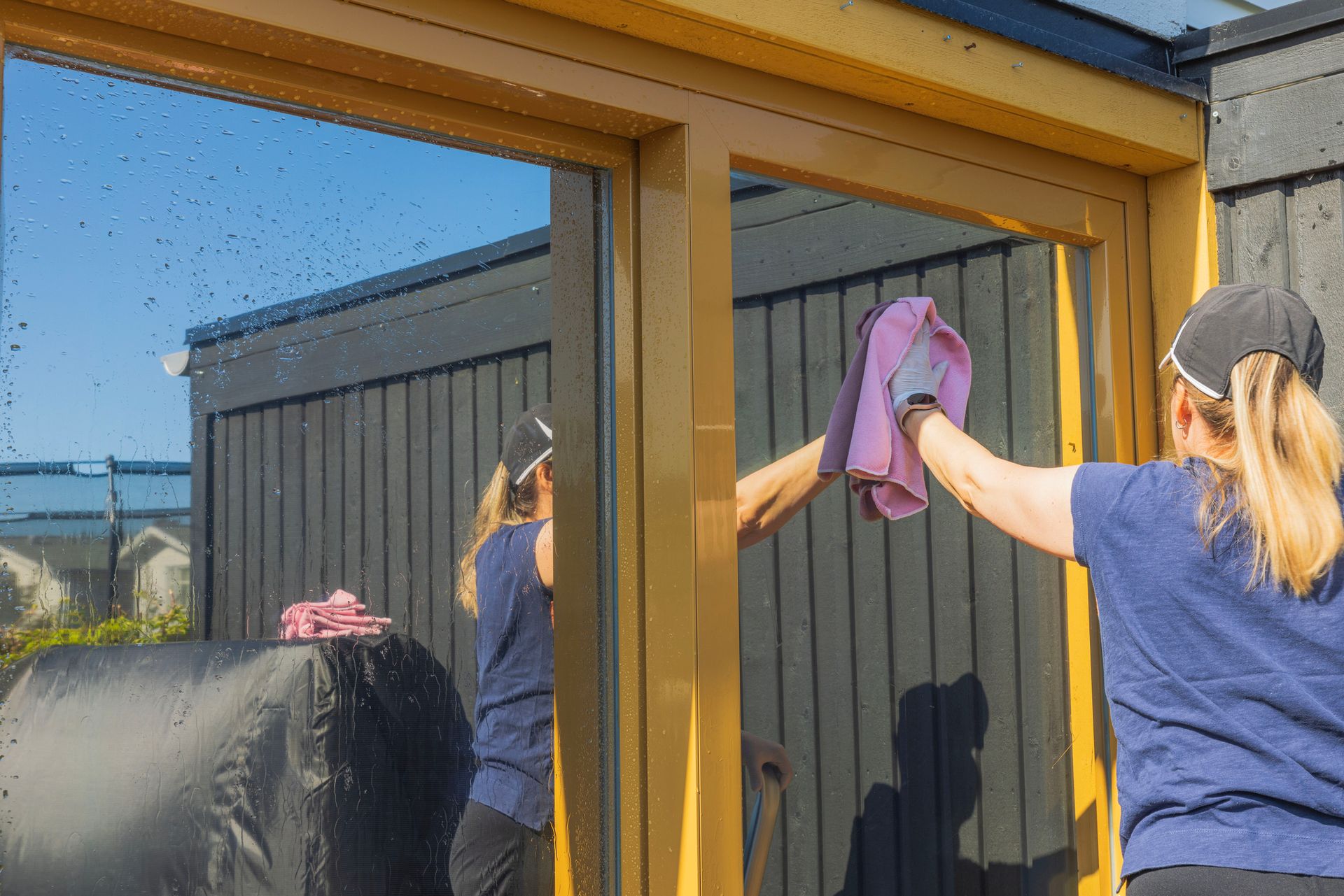 Gloved hands cleaning a window with a blue cloth and spray bottle