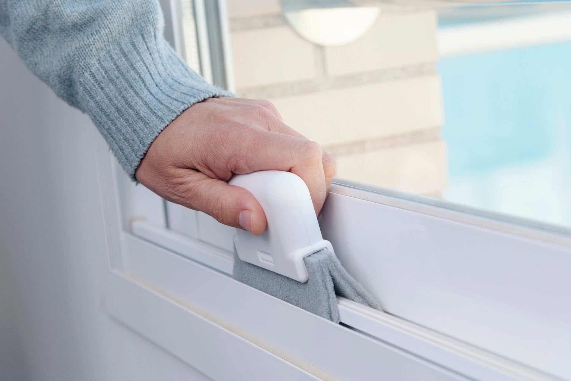 Hand gripping a white window lock on a white frame near a bright window
