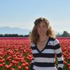 Woman smiling in striped shirt, standing in a field of red tulips with mountains in the background.