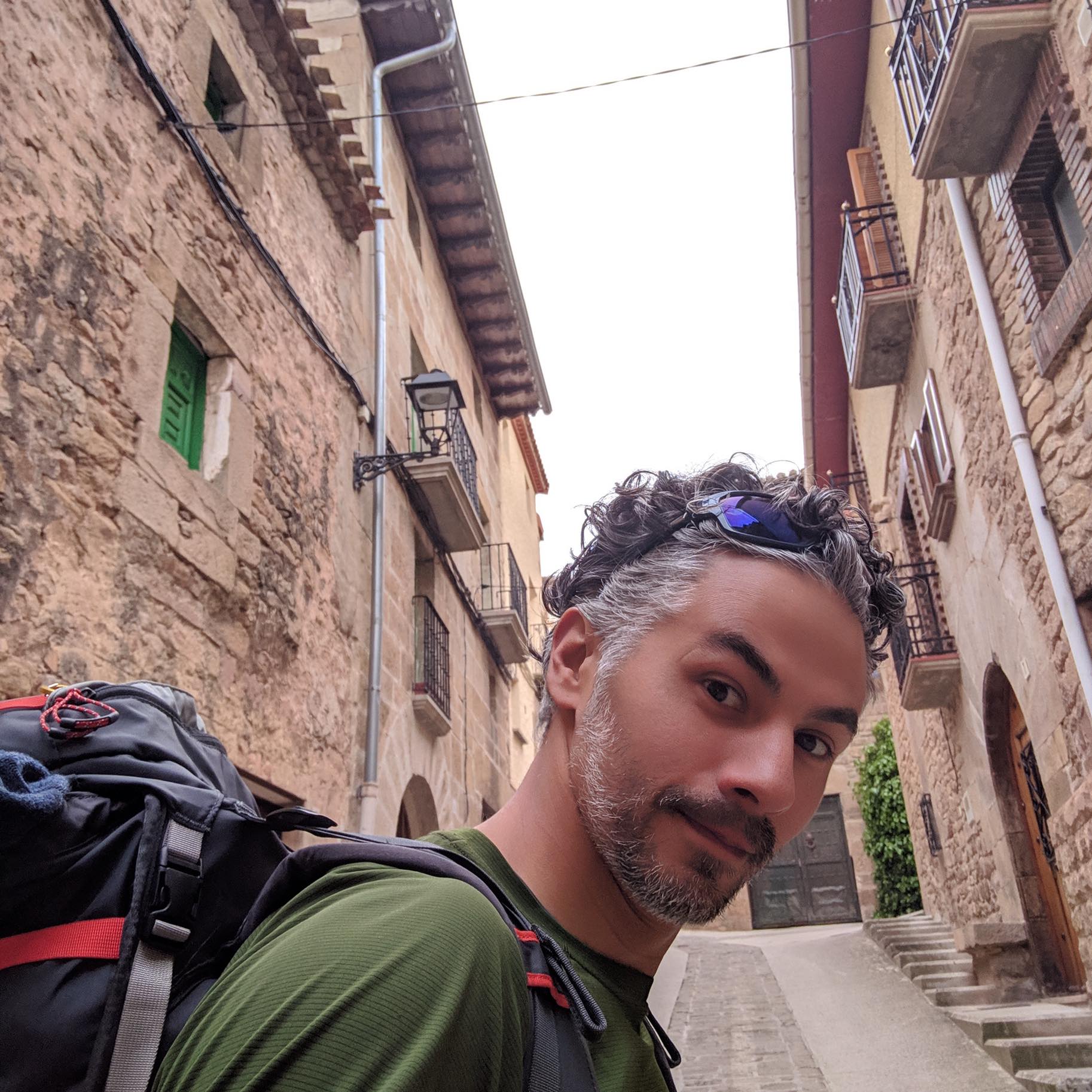 Man with backpack in narrow stone street, looking at camera.