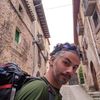 Man with backpack in narrow stone street, looking at camera.