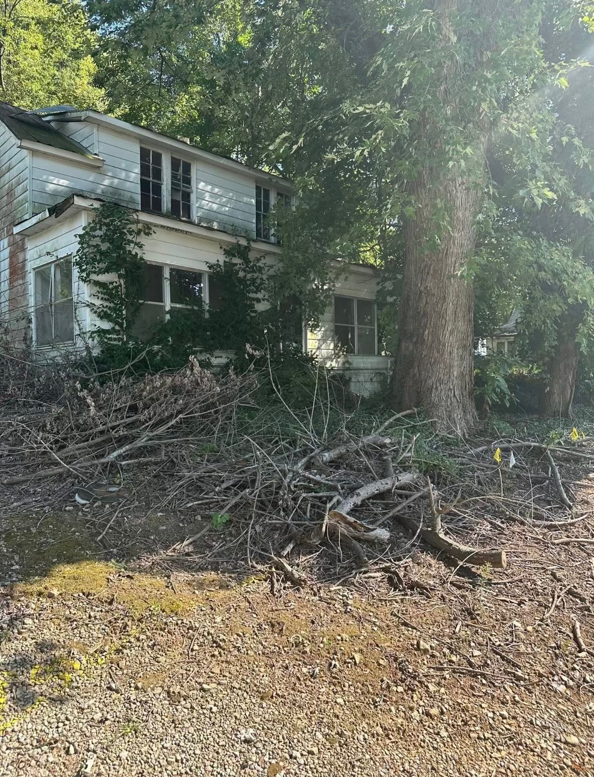 Old, overgrown house with peeling paint and broken windows, surrounded by trees and brush.