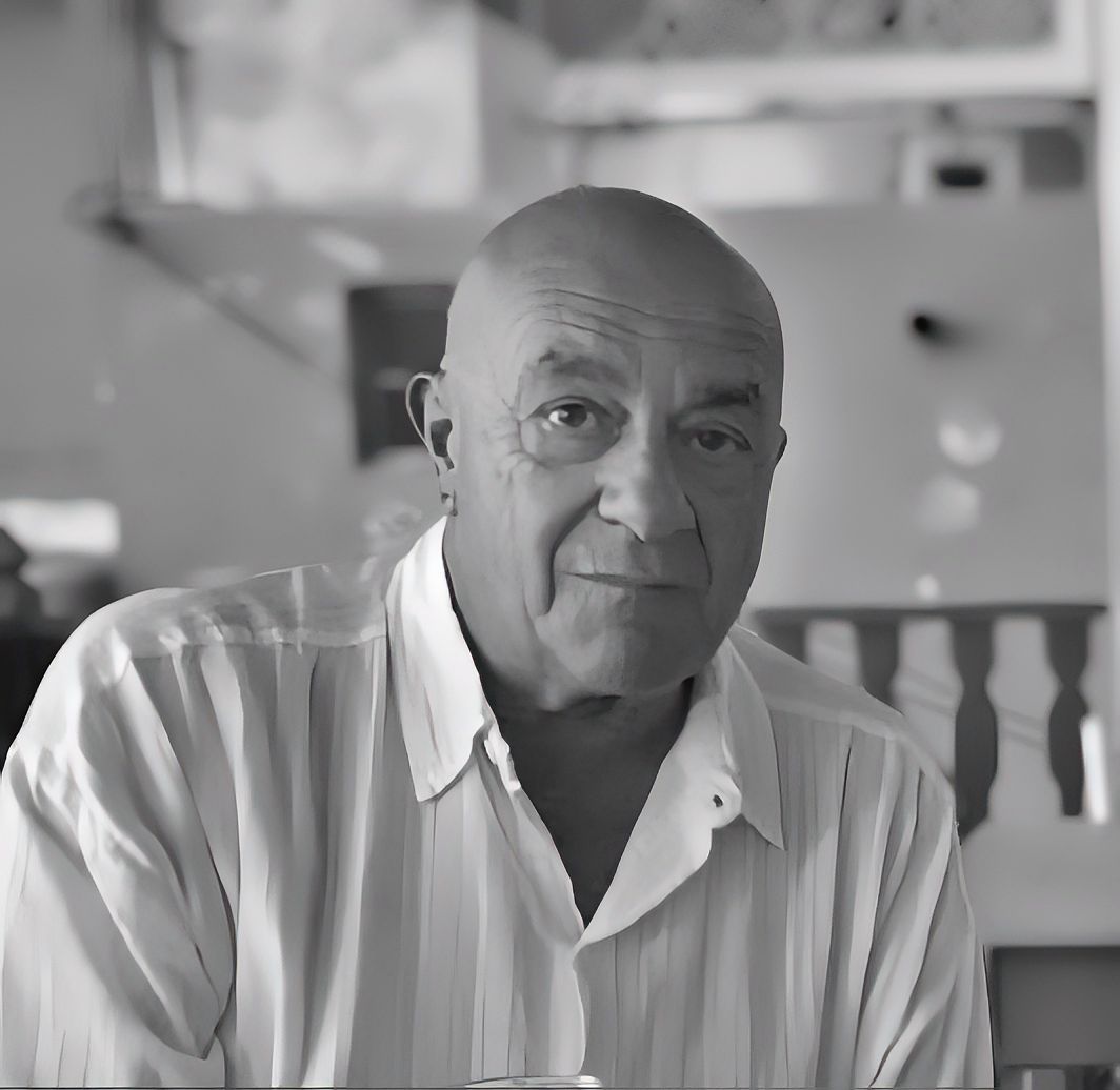 Un uomo con gli occhiali e un dolcevita nero sorride alla telecamera