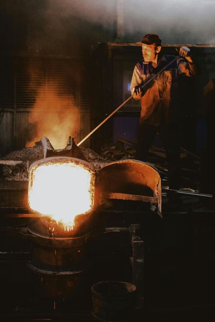 Un obrero remueve metal fundido en una fundición, con llamas de color naranja brillante y la luz incandescente del horno.
