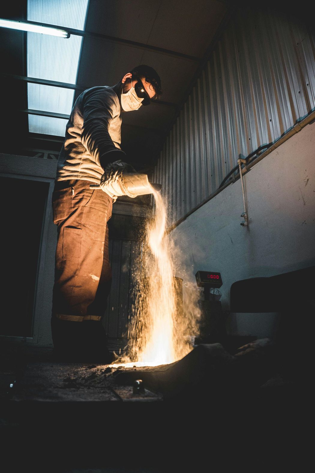 Un trabajador soldando metal en un taller con poca luz, saltando chispas al suelo.