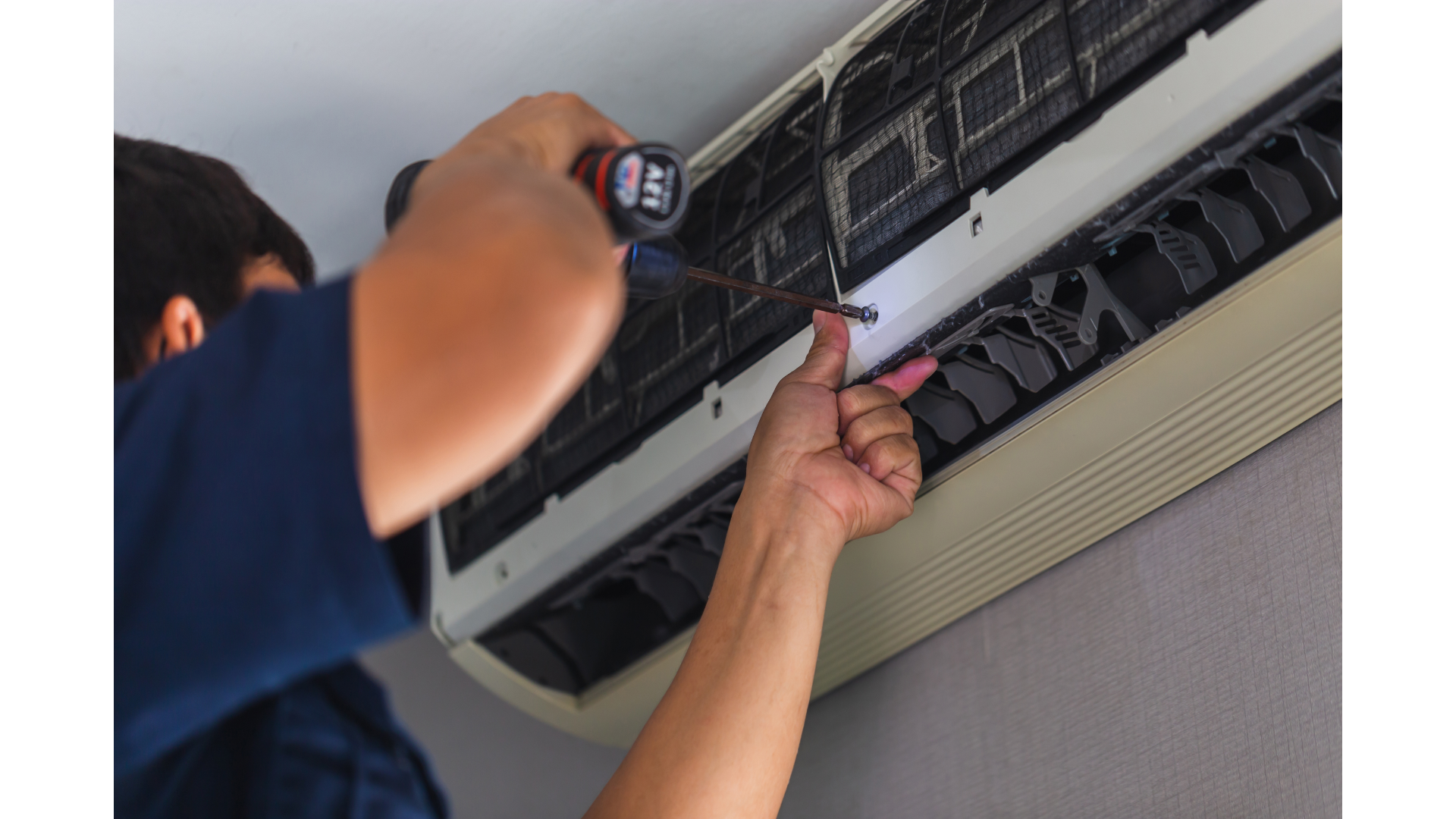 A man is fixing an air conditioner with a screwdriver.